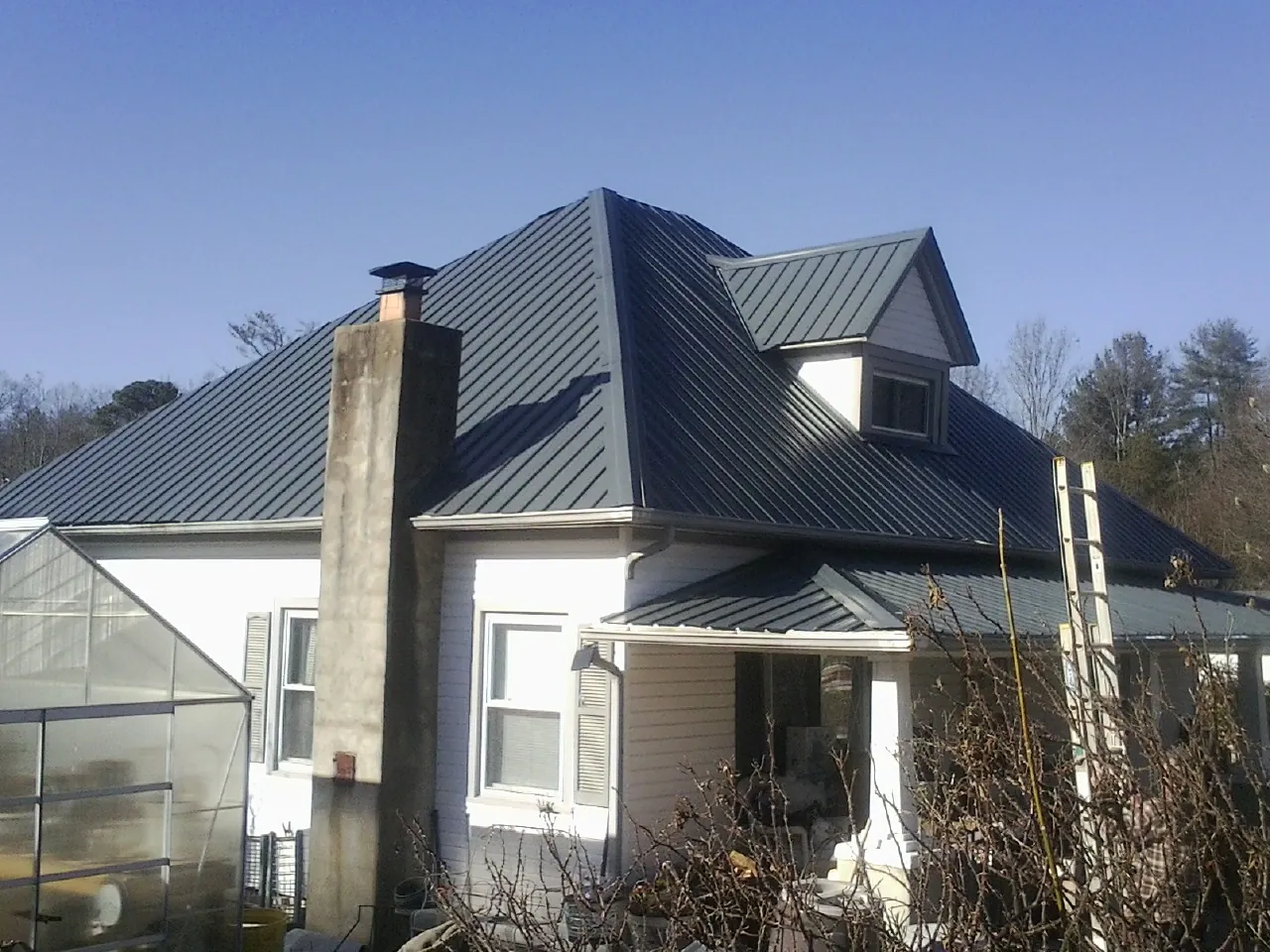 Dark blue standing seam metal roof on a white farmhouse with dormer — Slate & Tile Roof Repair by Roofing Brothers in Mastic Beach