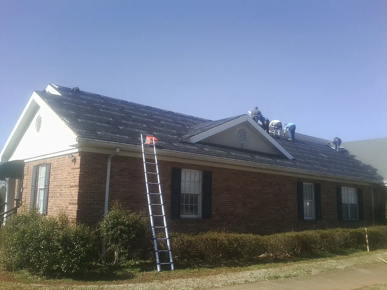 Crew tearing shingles off a brick ranch roof with a ladder set — Metal Roof Repair work by our crew in Mastic Beach