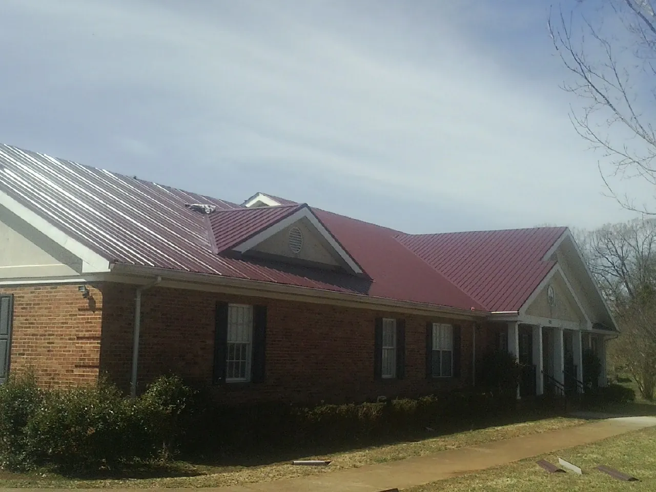 Red metal roof with gabled entries on a long brick building, from a Hail Damage Roof Repair job in Mastic Beach