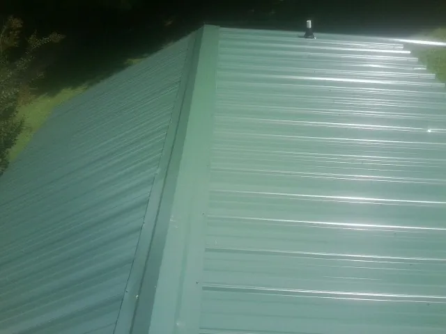 New green metal panels meeting at the ridge of a roof — Flat Roof Repair work by our crew in Mastic Beach