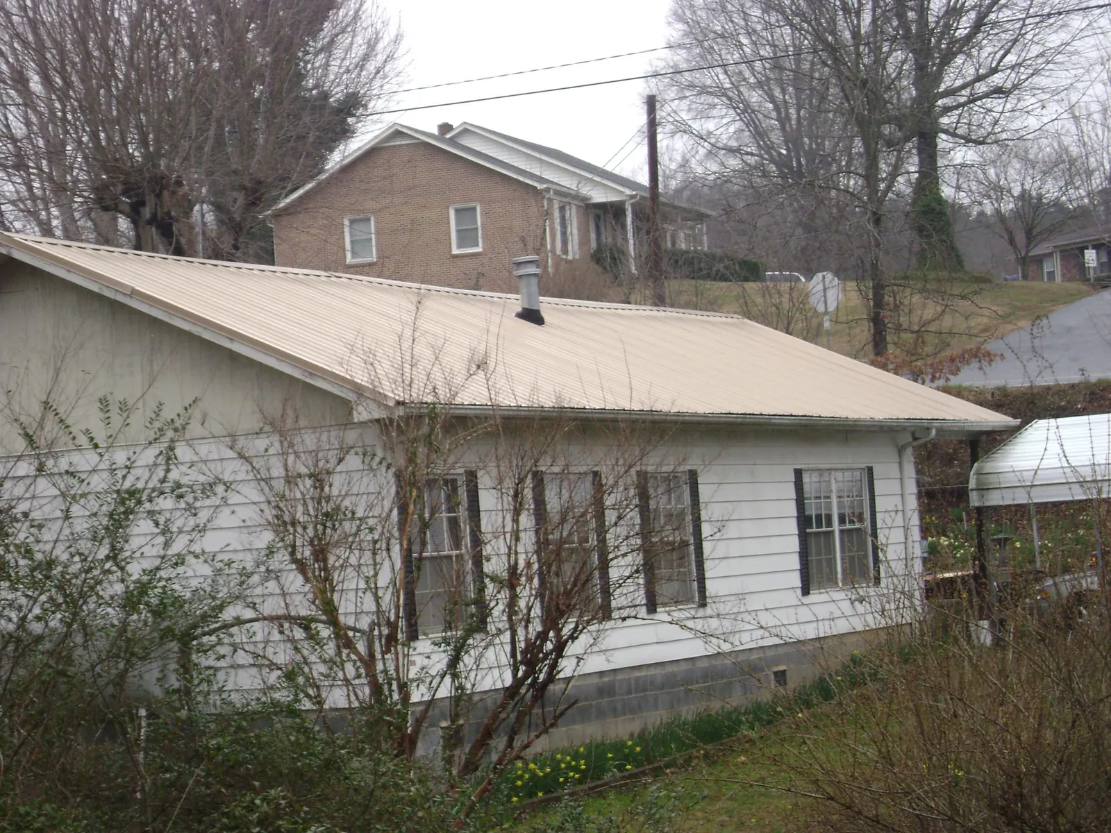 Tan metal roof on a white sided house set into a hillside — Commercial Roofing by Roofing Brothers in Mastic Beach