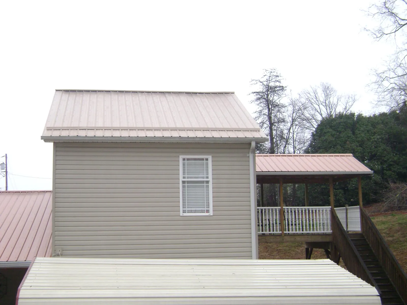 Tan metal roofs on a two story addition and attached porch, from a Roof Replacement job in Mastic Beach