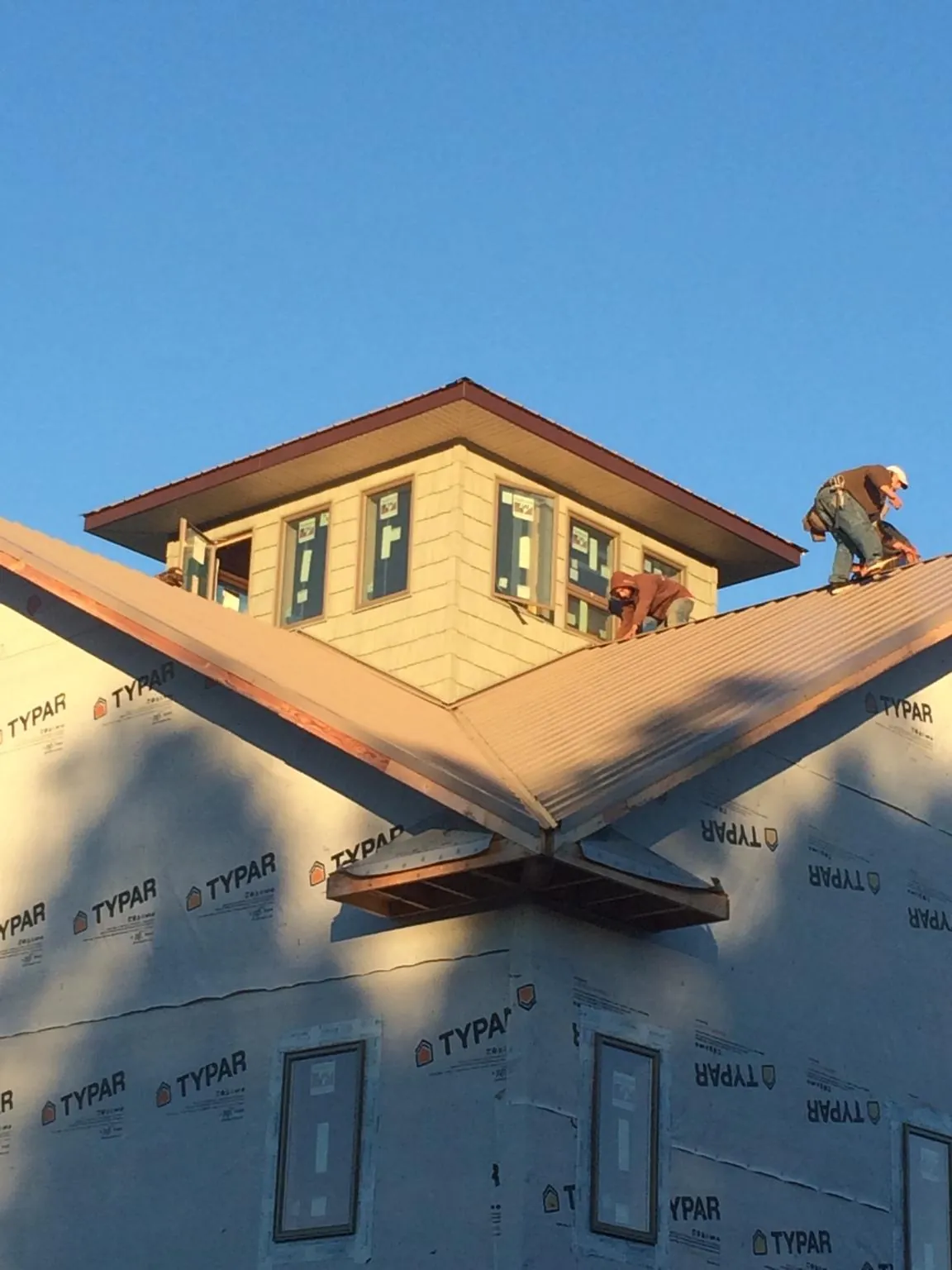 Roofers working around a rooftop cupola on a new metal roof at sunset — Roof Waterproofing in Mastic Beach by Roofing Brothers